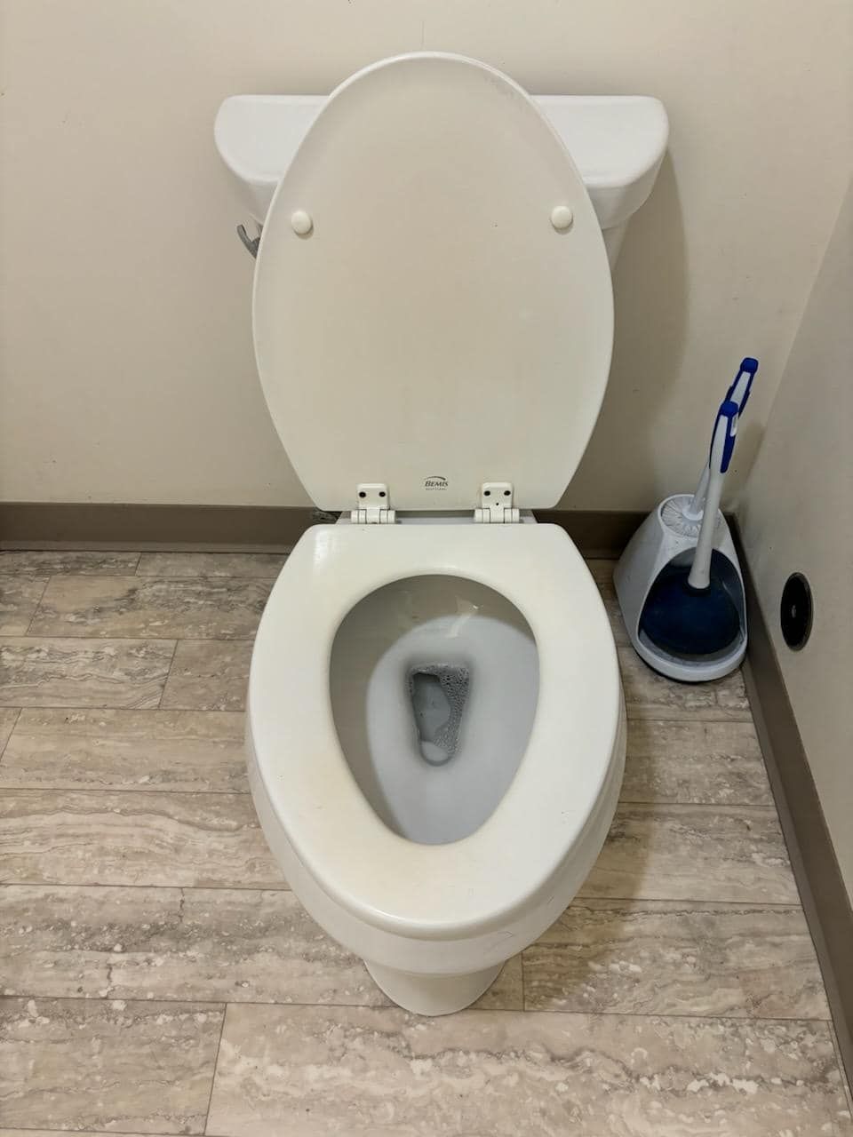 White toilet with the lid open, a toilet brush is next to it on a light wood floor.