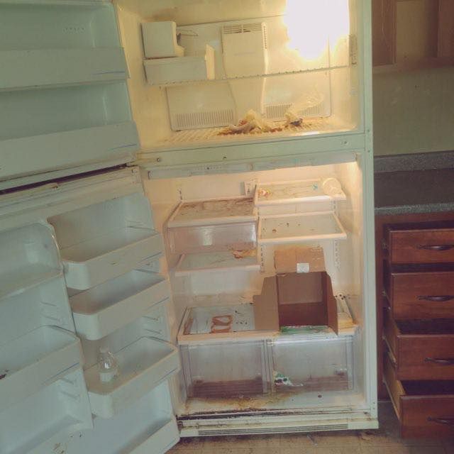 Open, dirty refrigerator with empty shelves and debris inside.
