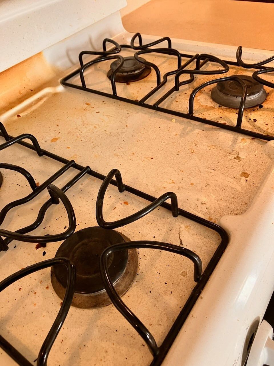 Dirty white gas stovetop with black grates and burners.
