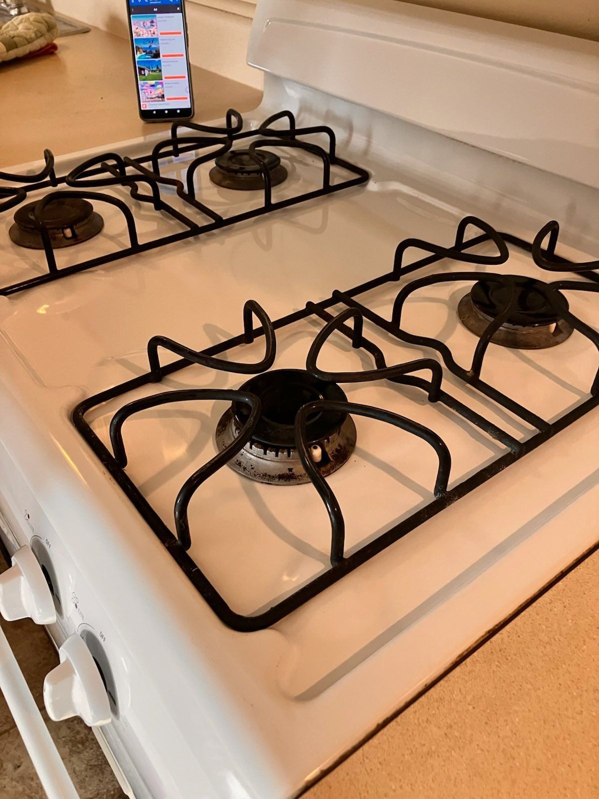 White gas stovetop with black grates; phone on back.