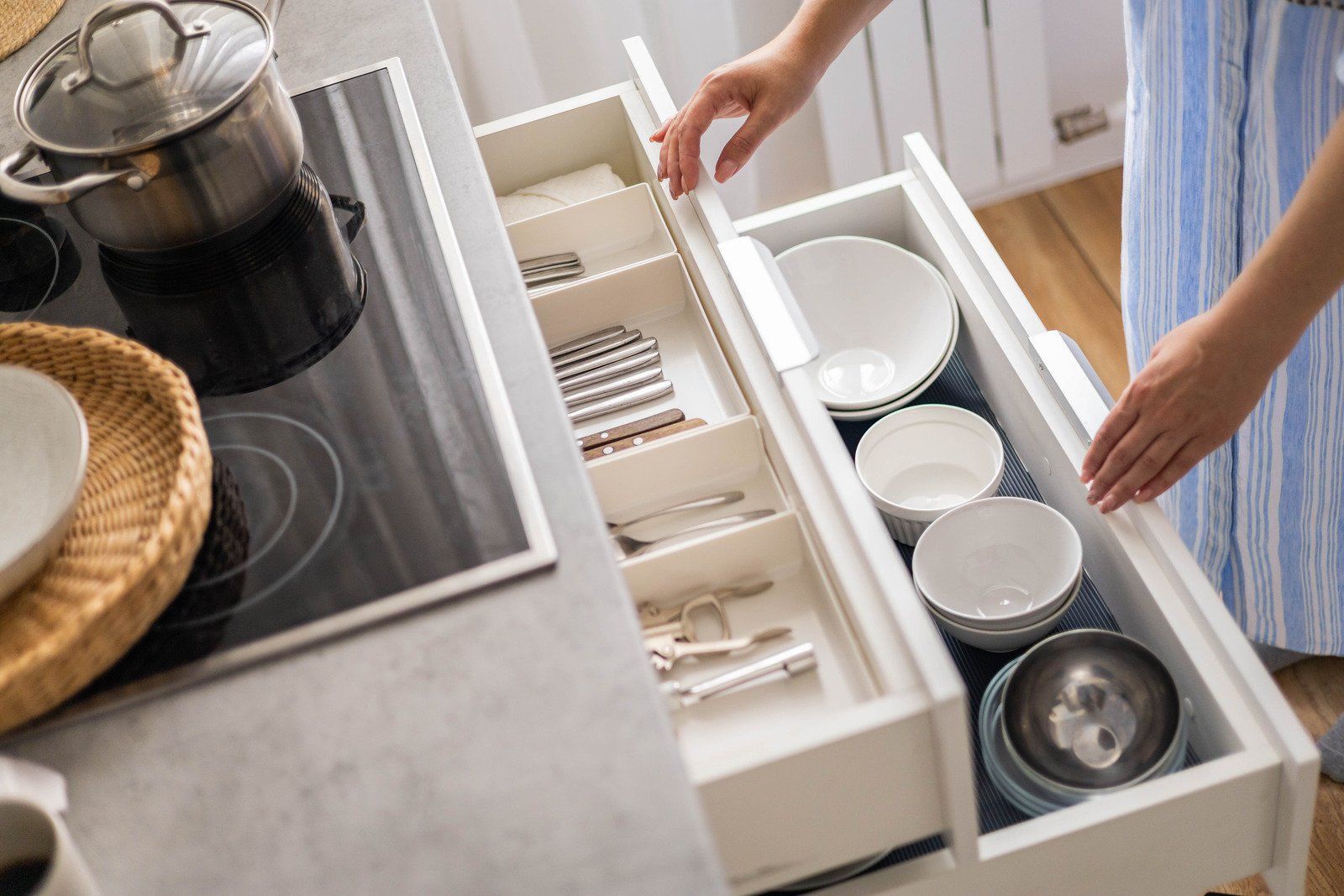 Person opening kitchen drawers containing utensils and bowls.