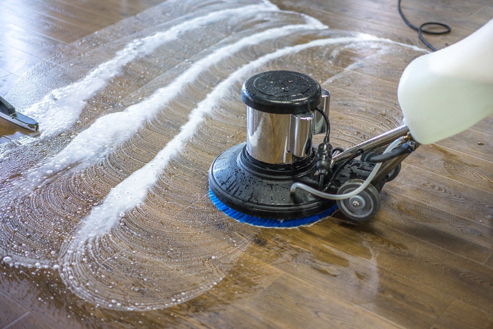 Floor cleaning machine scrubbing a wooden floor, creating sudsy cleaning patterns.