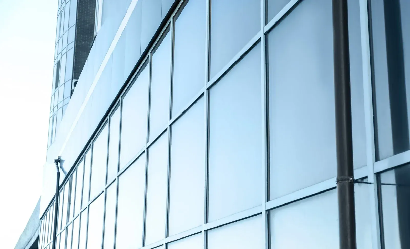 Glass facade of a modern office building, reflecting sky and adjacent structures.