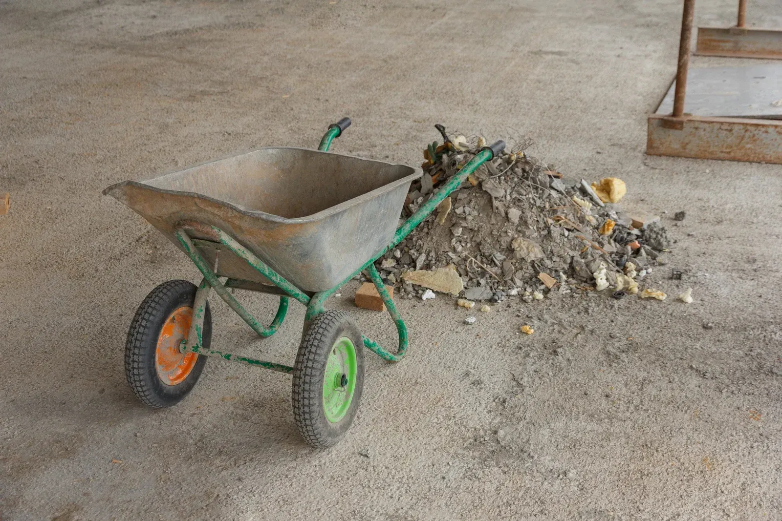 Wheelbarrow next to a pile of debris on a concrete surface.
