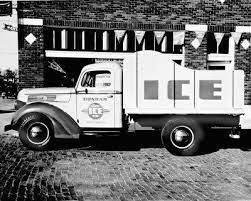 A black and white photo of an old ice truck parked in front of a brick building.