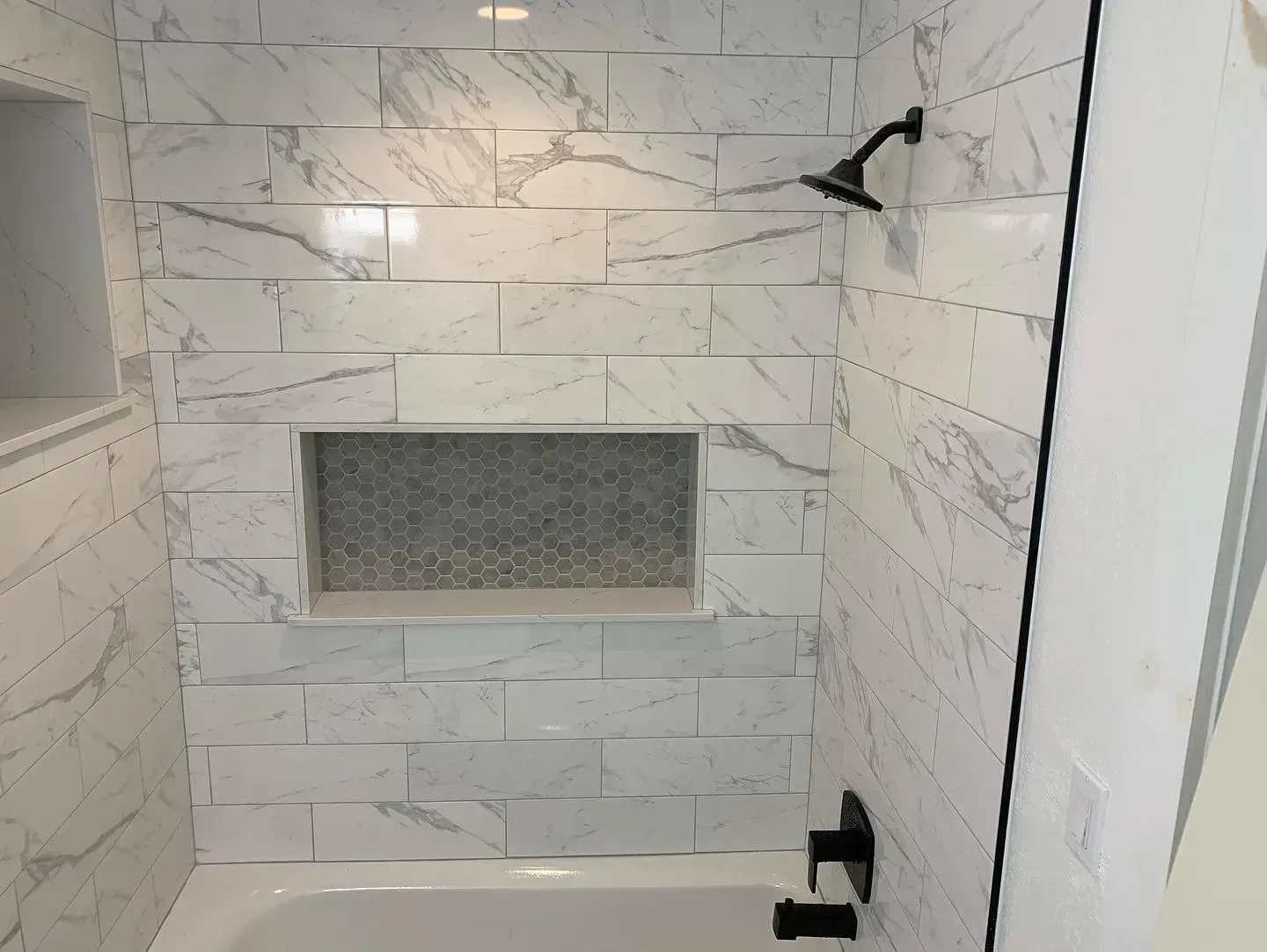 White tiled walk-in shower with a recessed shelf, black fixtures, and a glass door frame