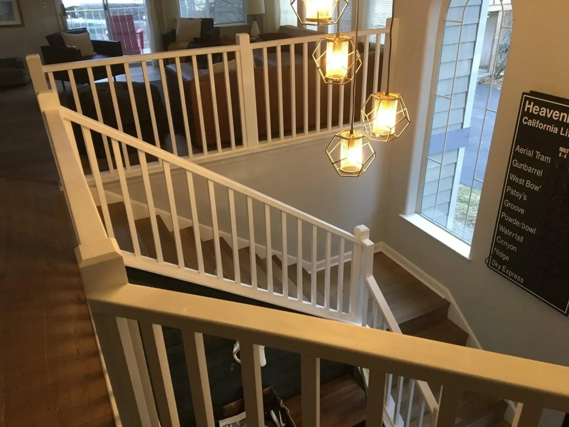 Indoor stairwell with white railings, hanging lanterns, and large windows overlooking a brick exterior