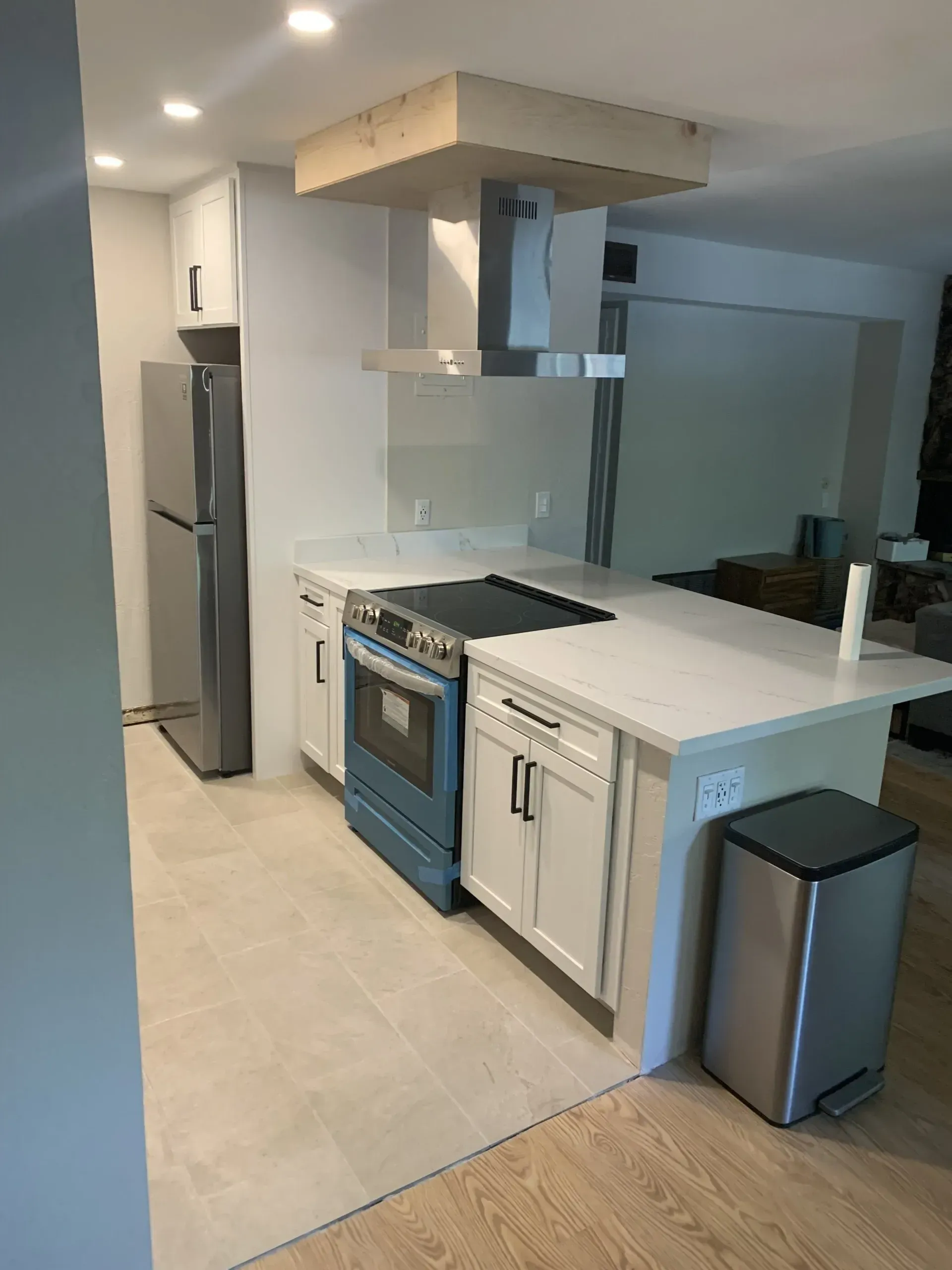Modern kitchen with white cabinets, blue oven, stainless fridge, island, and two trash bins.