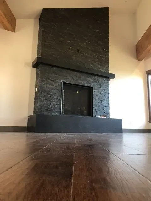 Empty living room with a large stone fireplace and wooden floor, viewed from a low angle