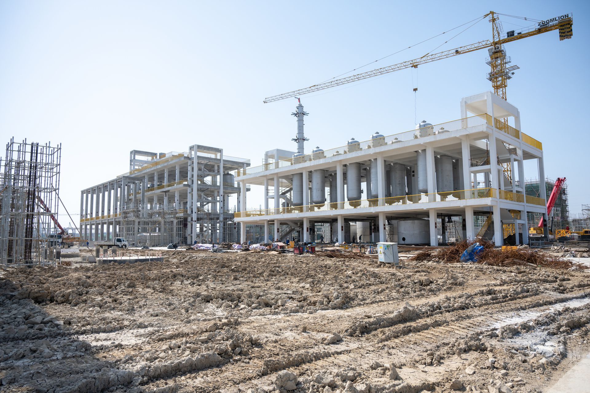 A large building is being built in a dirt field with a crane in the background.