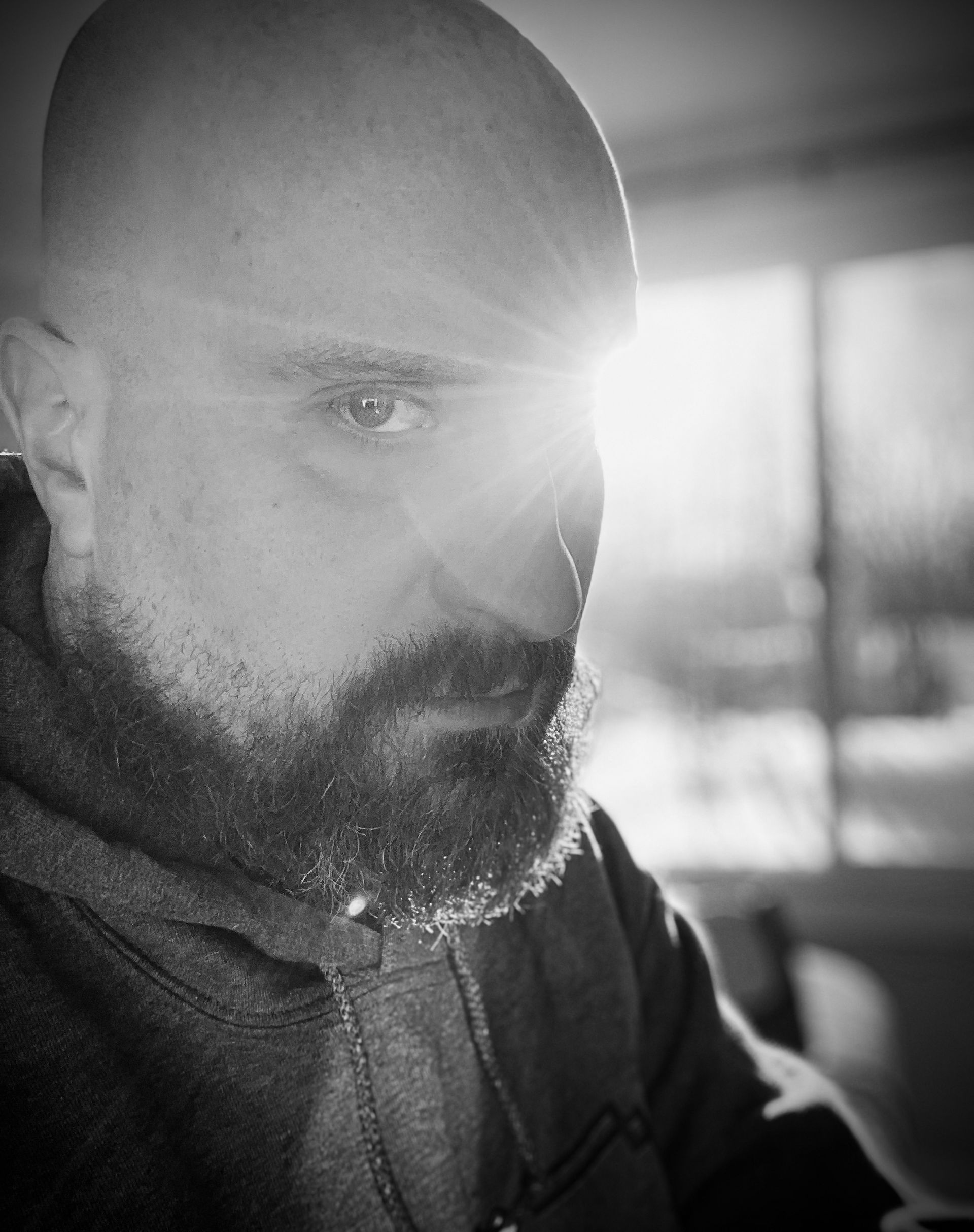 A bald man with a beard is looking at the camera in a black and white photo taken by Ever After Studio.
