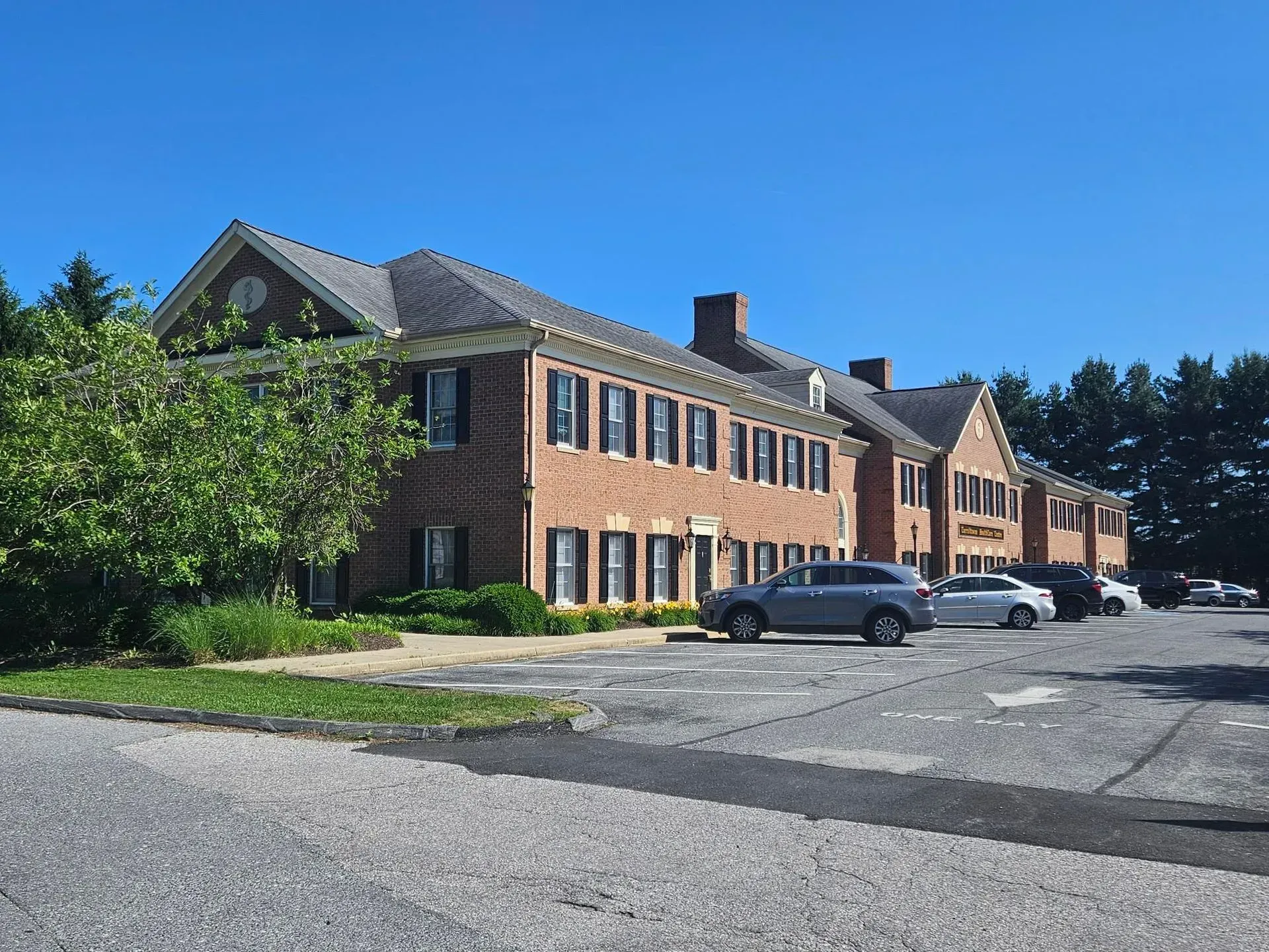 Brick office building with parked cars beside a paved lot under a clear blue sky