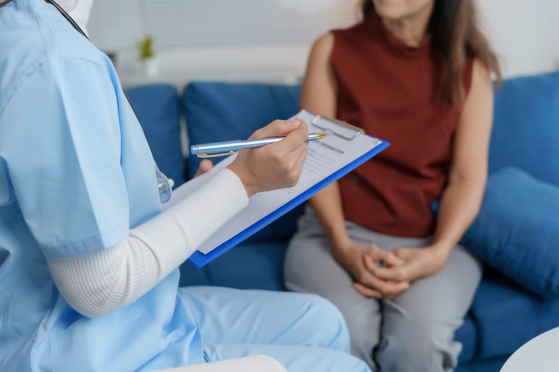 Therapist taking notes while speaking with a seated client on a blue couch Therapist taking notes while speaking with a seated client on a blue couch