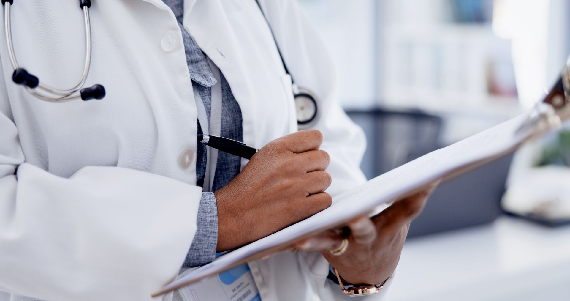 Doctor in white coat writing on a clipboard with a stethoscope around the neck