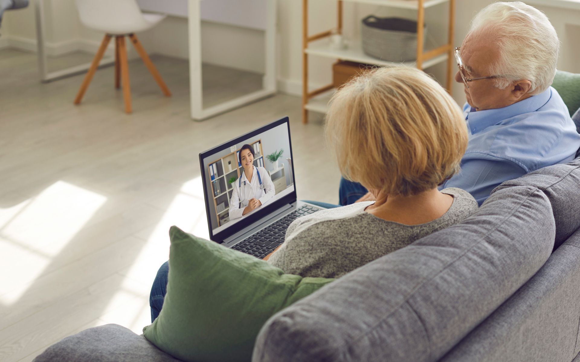 Two people on a couch watching a video call on a laptop in a bright living room Two people on a couch watching a video call on a laptop in a bright living room