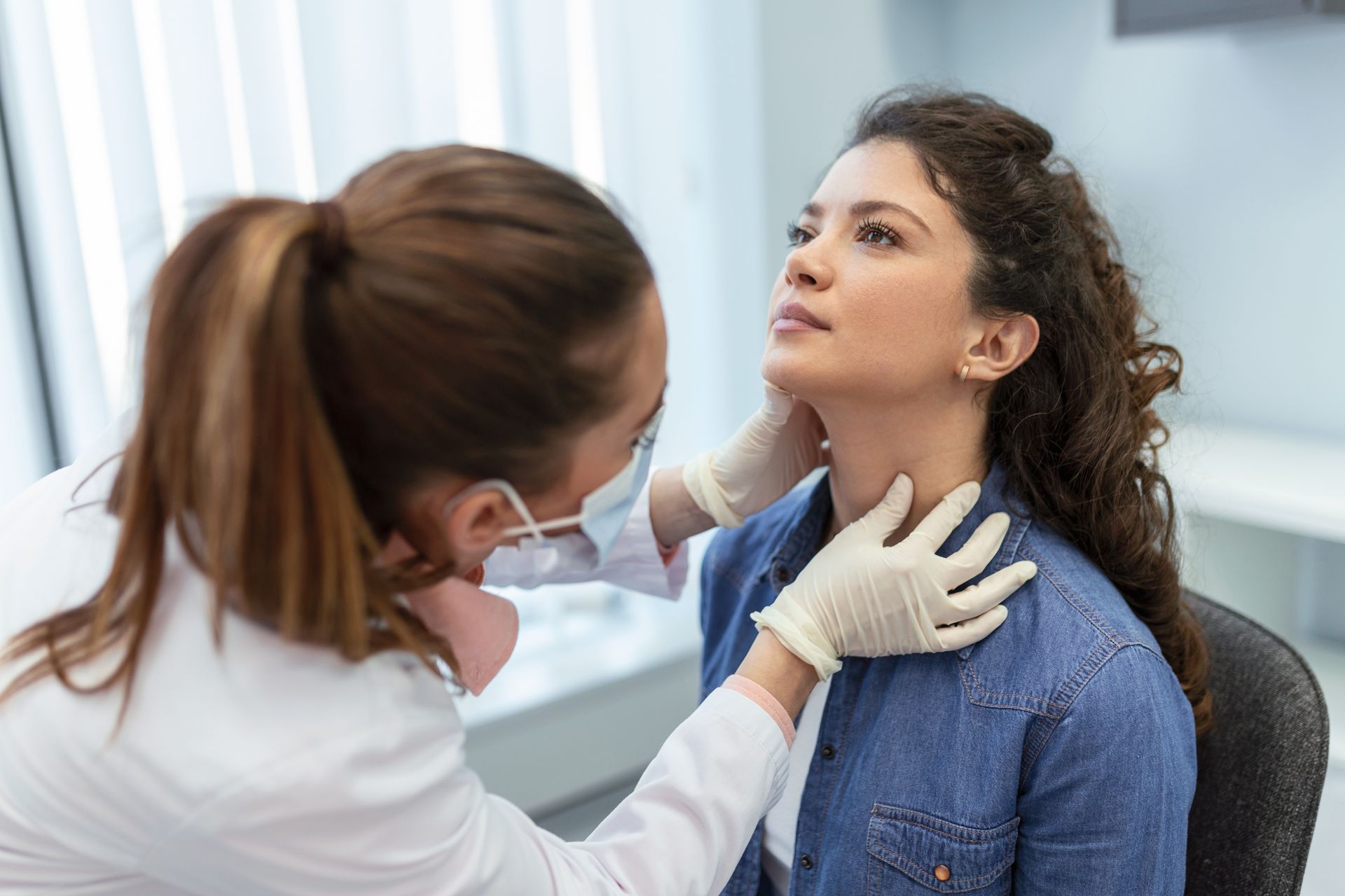 Doctor examining a patient’s neck in a bright clinic office Doctor examining a patient’s neck in a bright clinic office
