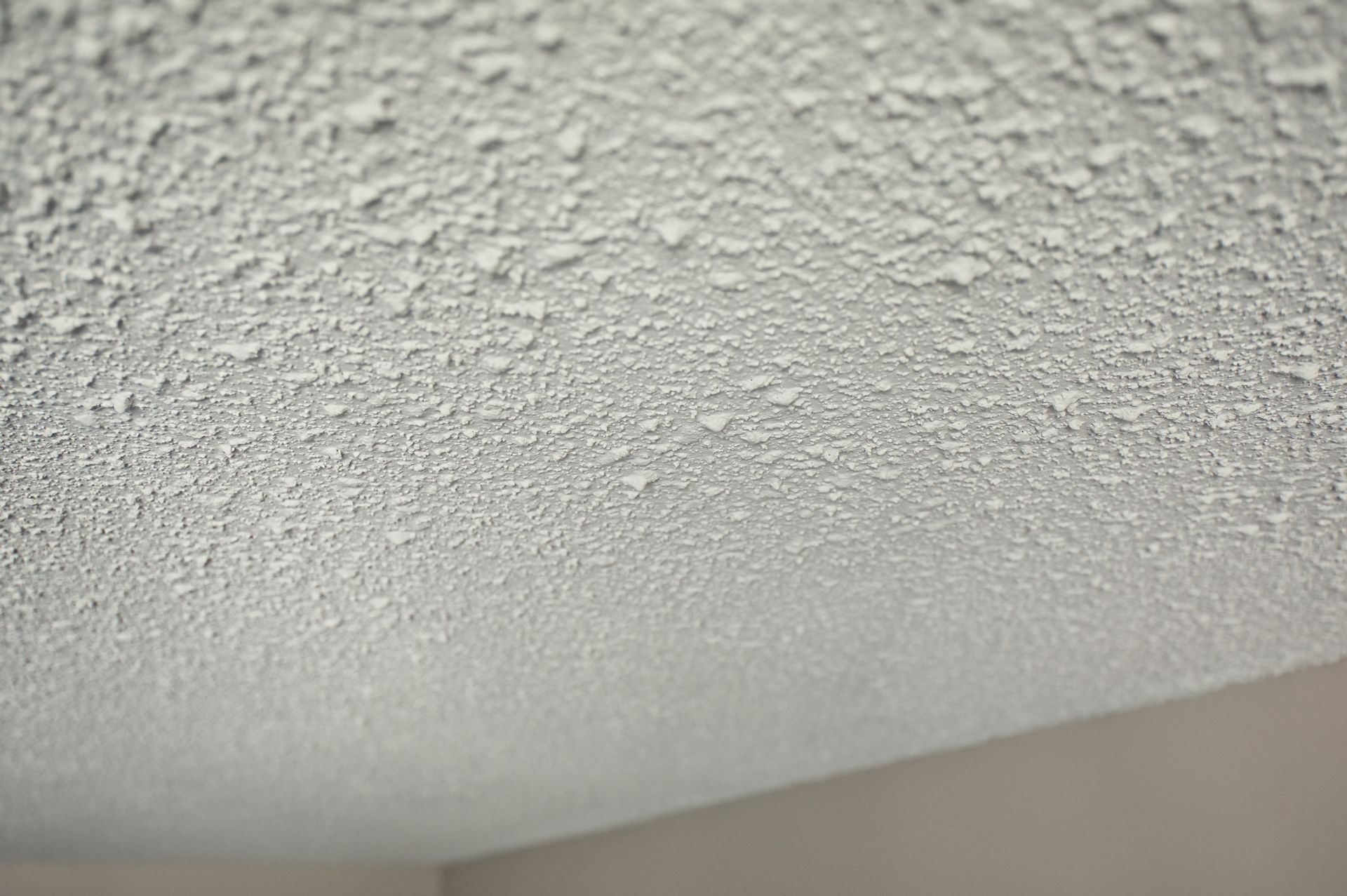 White popcorn-textured ceiling meeting a beige wall at a corner