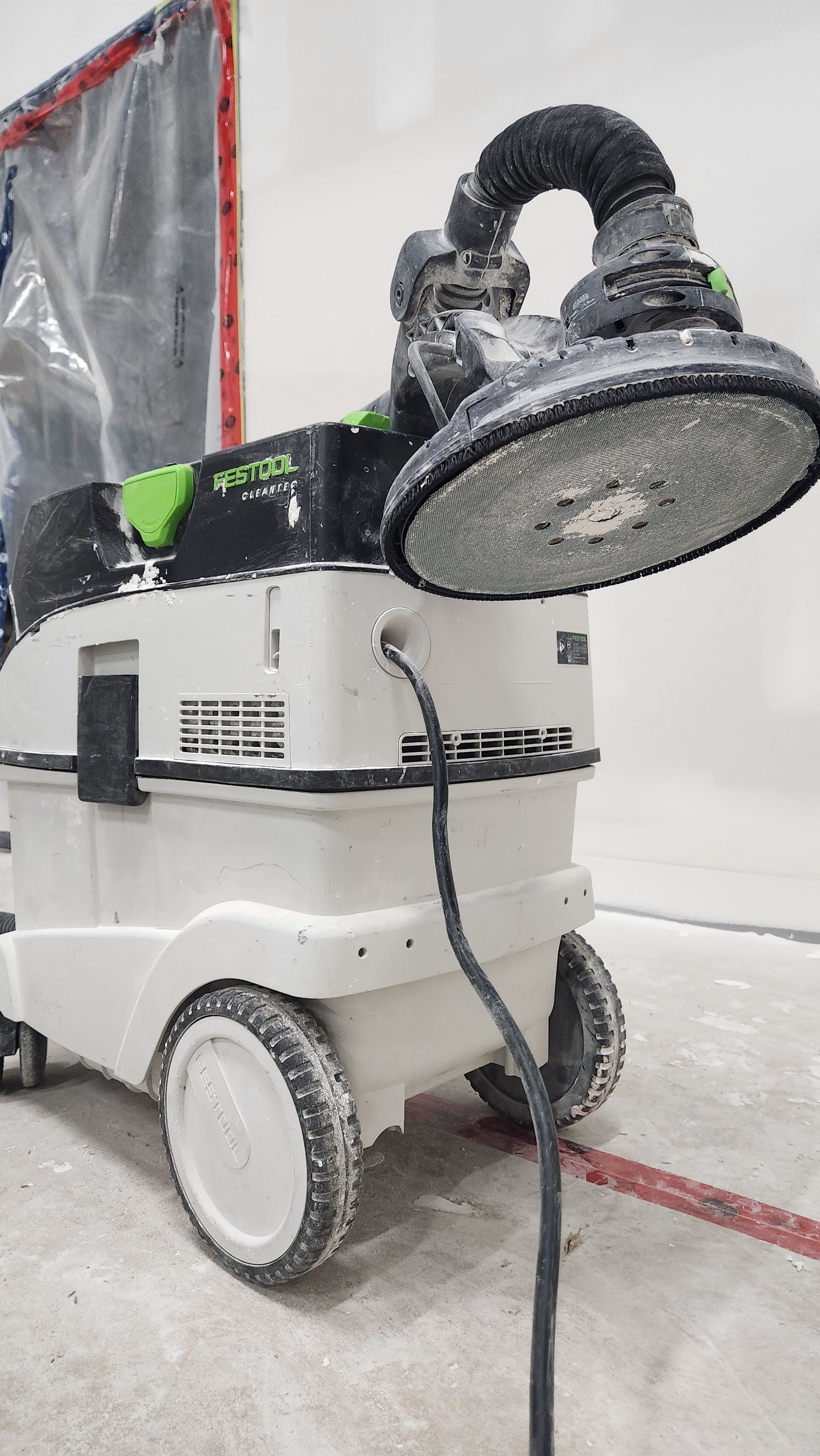 White dust extractor with attached sanding head. Used in a dusty interior setting.
