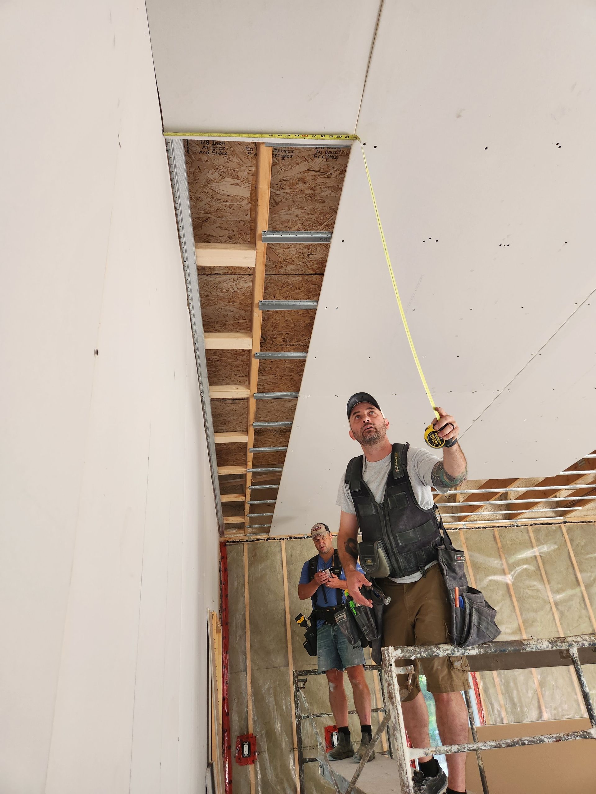 Two people measuring ceiling height during construction.