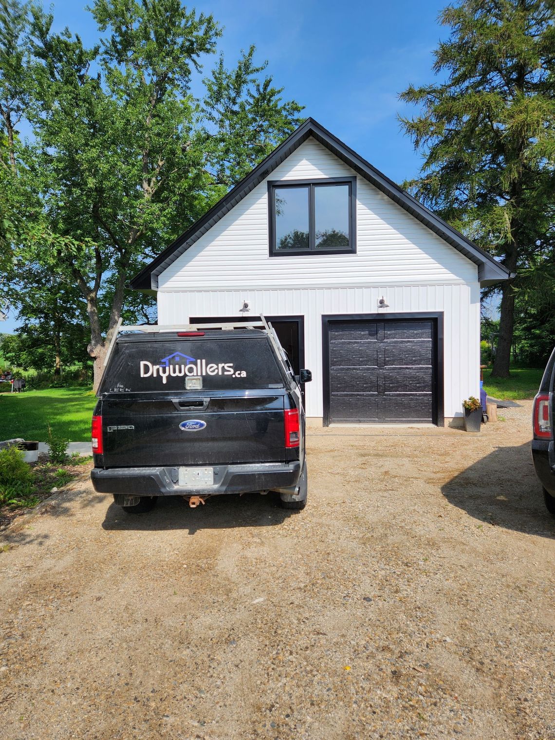 Black SUV parked in front of a white barn-like building with black trim, a garage door, and a window.
