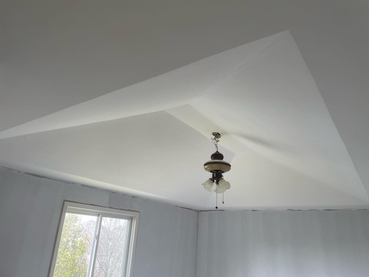 White ceiling with a recessed triangular shape and a hanging light fixture.