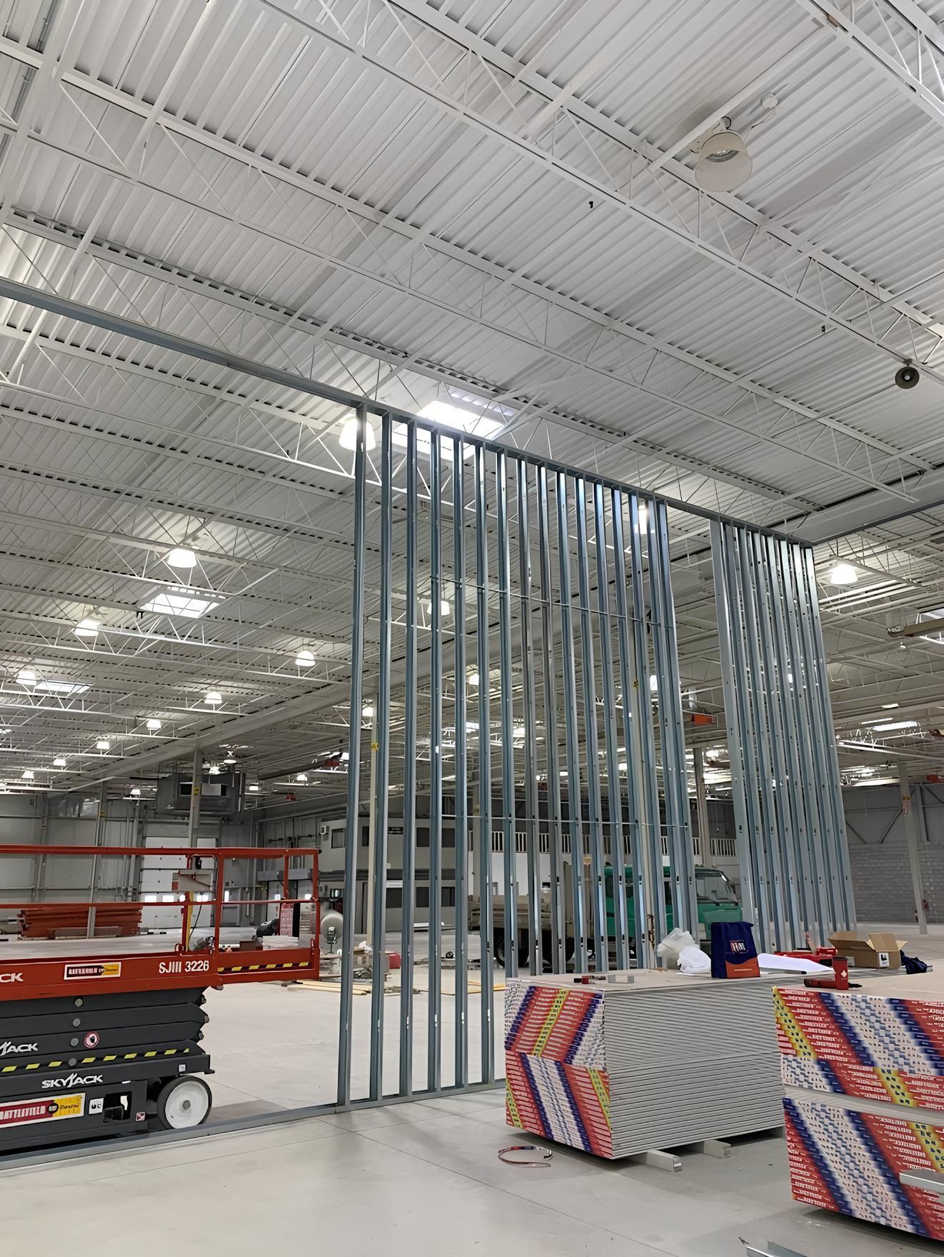 Metal stud framing for a wall under construction inside a large warehouse with high ceilings.