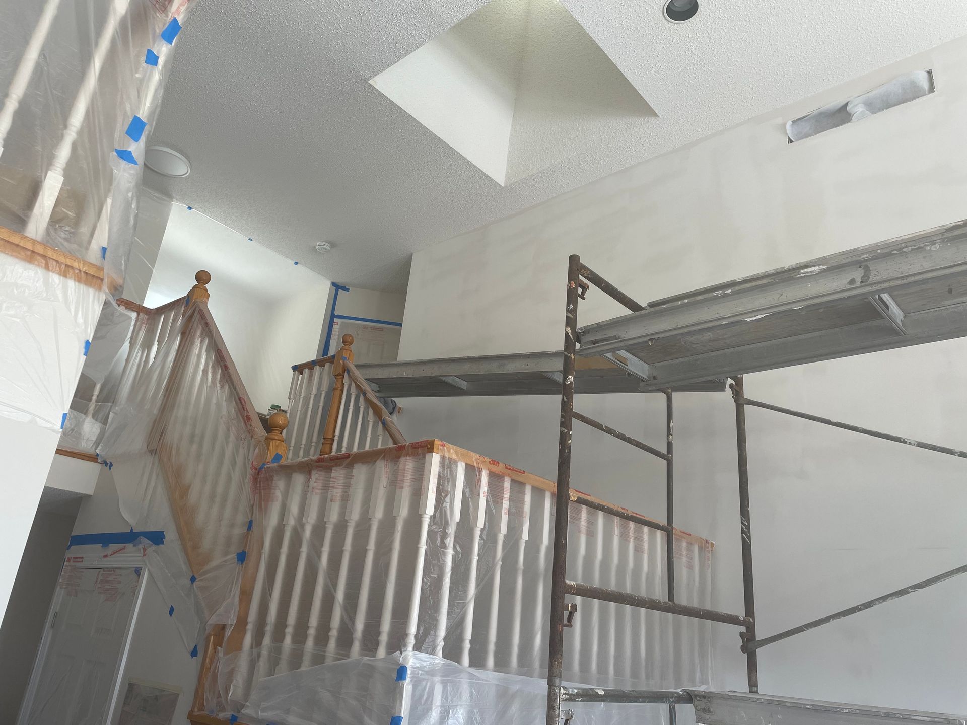 Interior view of a staircase and scaffolding, painted white. Protective plastic covers the staircase.