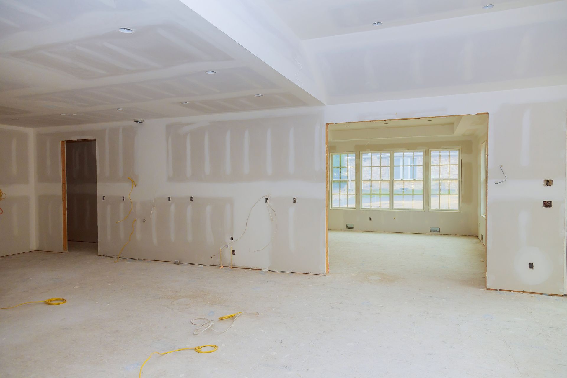 Empty unfinished room with white drywall, beige trim, and a large window opening