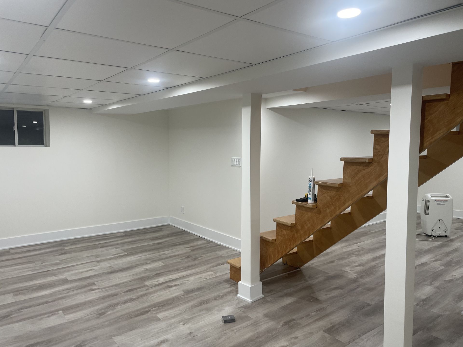 Basement interior with gray flooring, white walls, wood stairs, and recessed lighting.