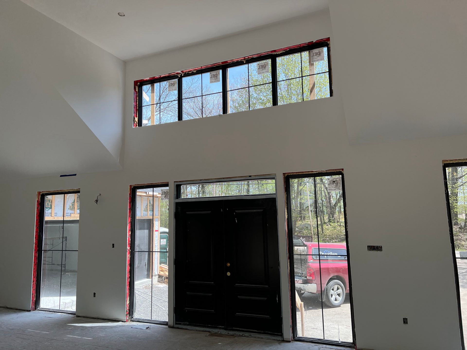 Interior of a modern house under construction; large black front door, tall windows, white walls.