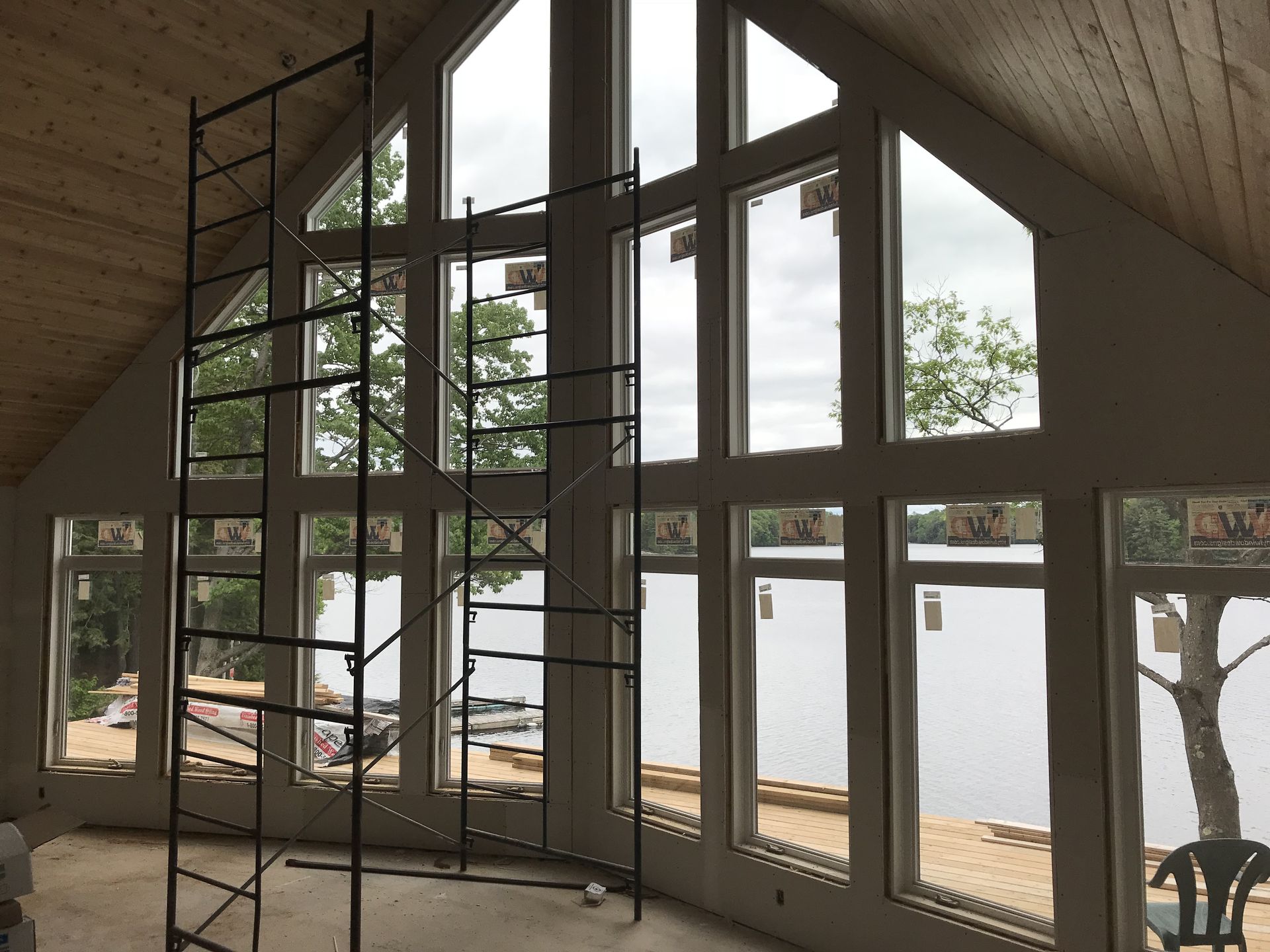 Interior with large windows overlooking a lake. A scaffolding is set up in front of the windows.