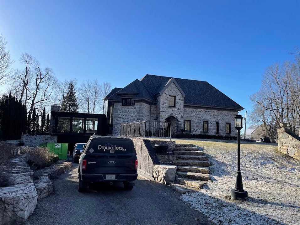 Gray stone house with black truck parked in driveway. Sunny day.