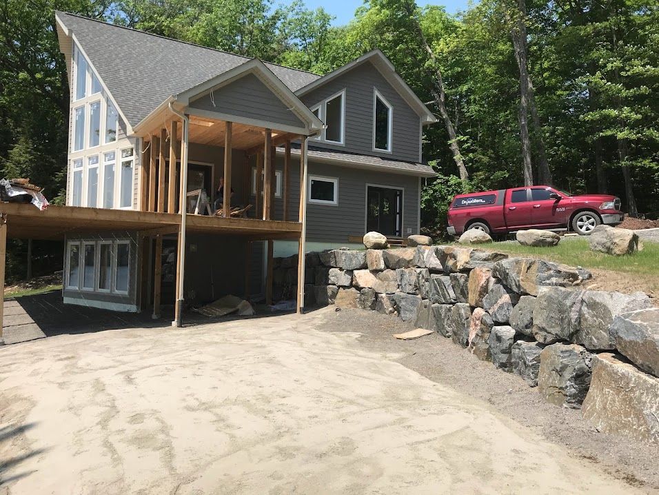 Gray house with a deck and stone retaining wall. Red truck parked on the right.