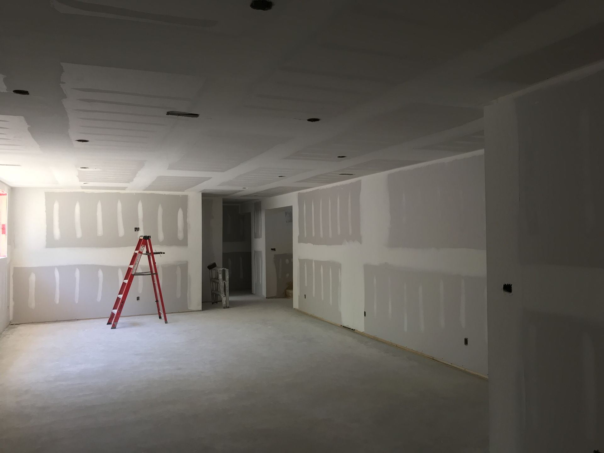 Interior construction site with drywall on walls and ceiling; red ladder in the middle.