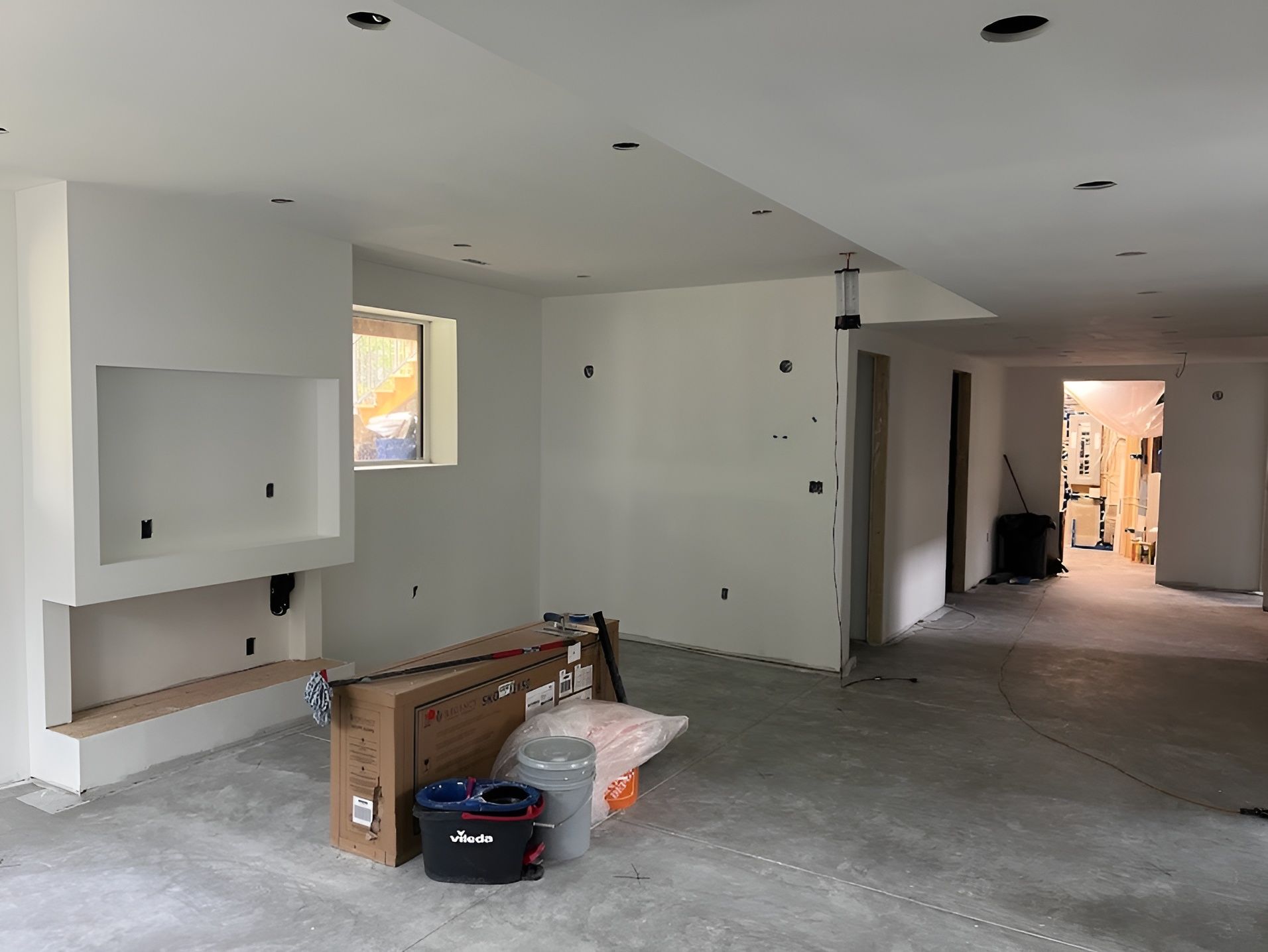 Interior of a room under construction, with white walls, fireplace, and exposed concrete floor.