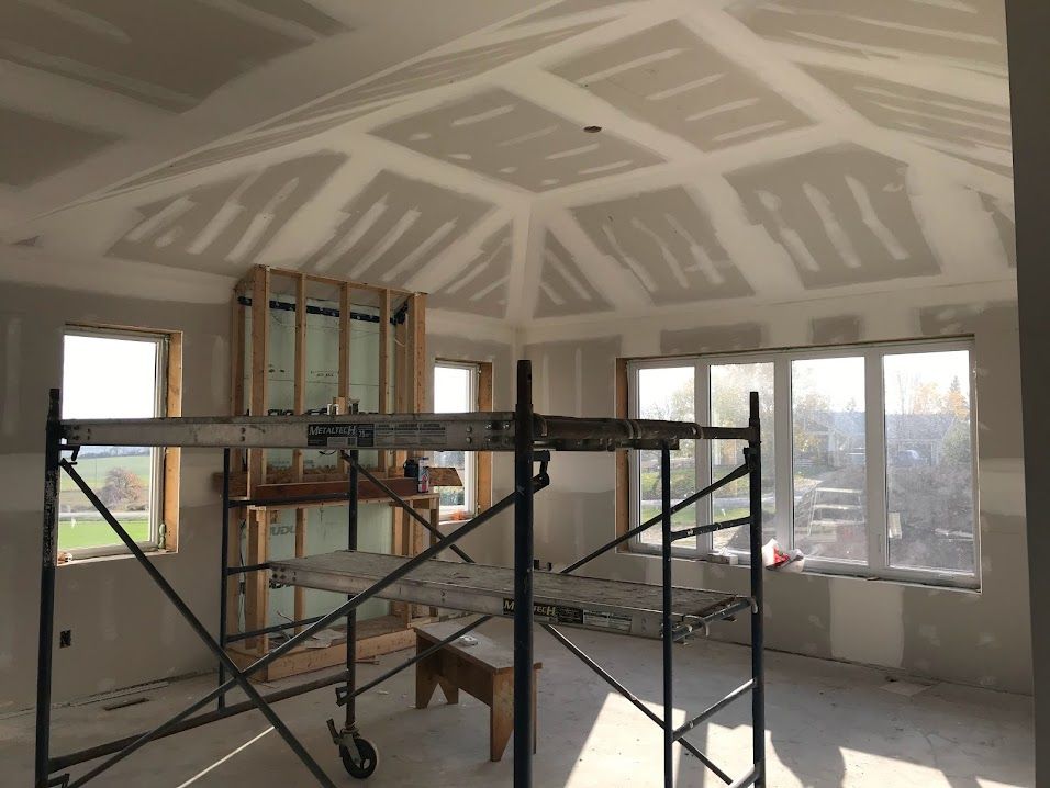 Interior view of a room under construction with drywall on the ceiling and walls. Scaffolding is set up.