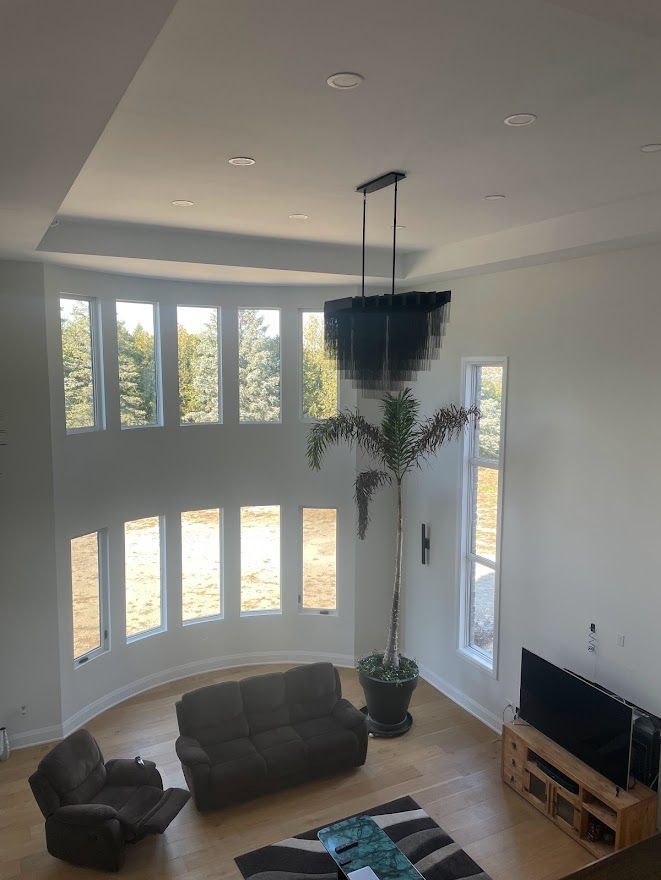A tall, light-filled living room with a large chandelier, windows, a couch, and a TV.