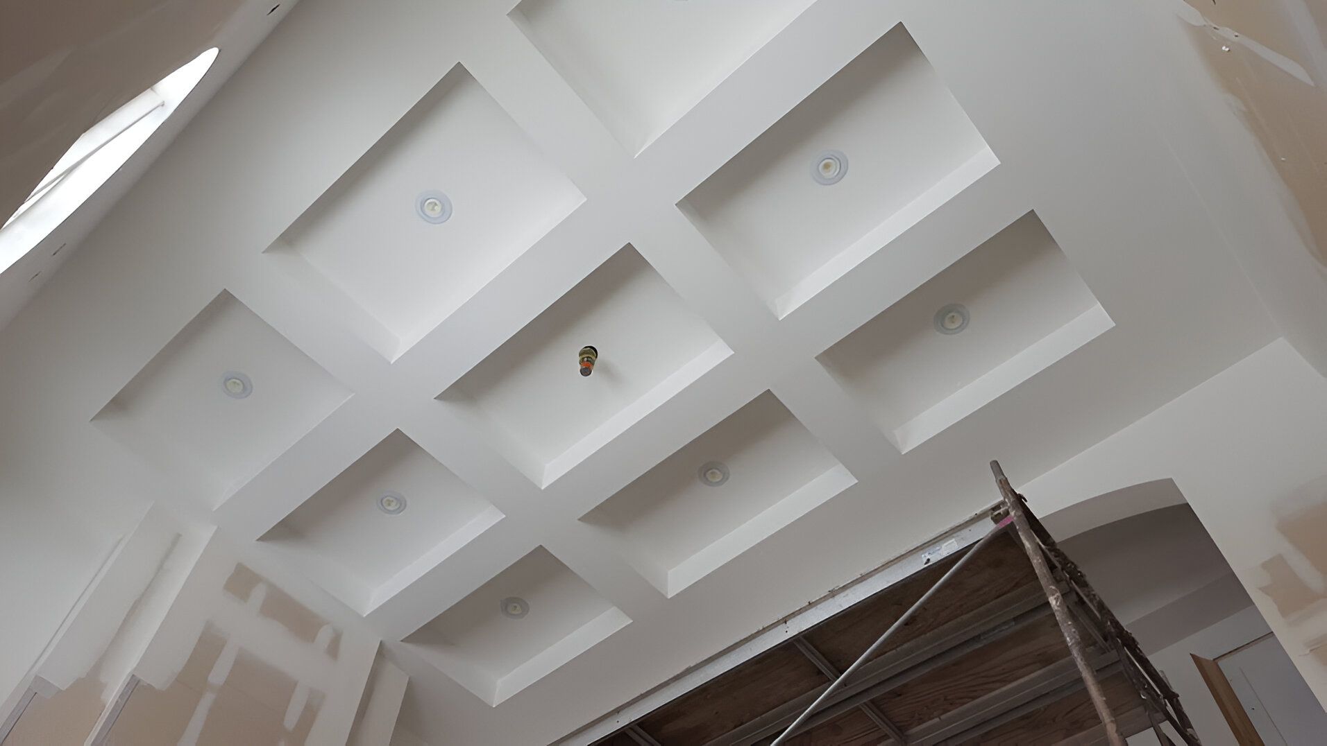 White ceiling with recessed square coffers, unfinished walls, and scaffolding.