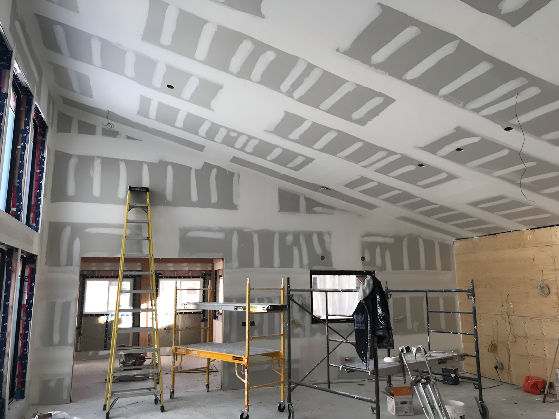 Interior construction: Drywall installed on angled ceiling, scaffolding and ladder present.