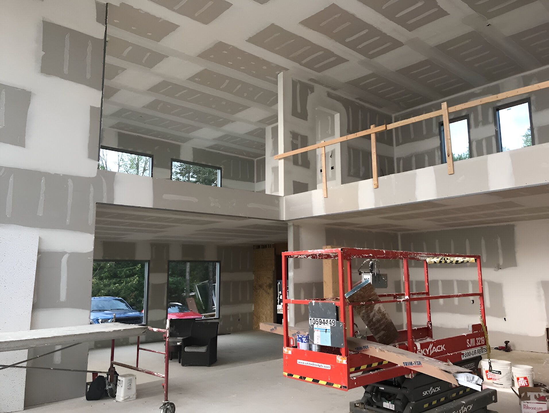 Interior of a house under construction. Drywall installed on walls and ceiling; lift and construction materials present.