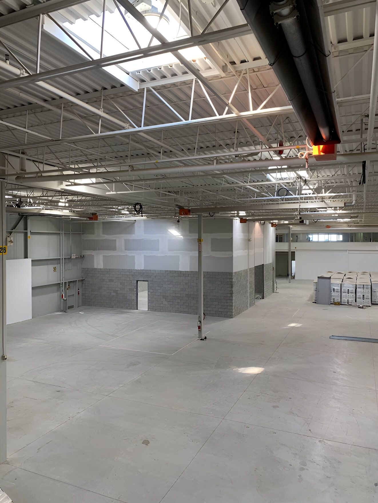 Empty industrial space with concrete floor and white walls, exposed metal beams.