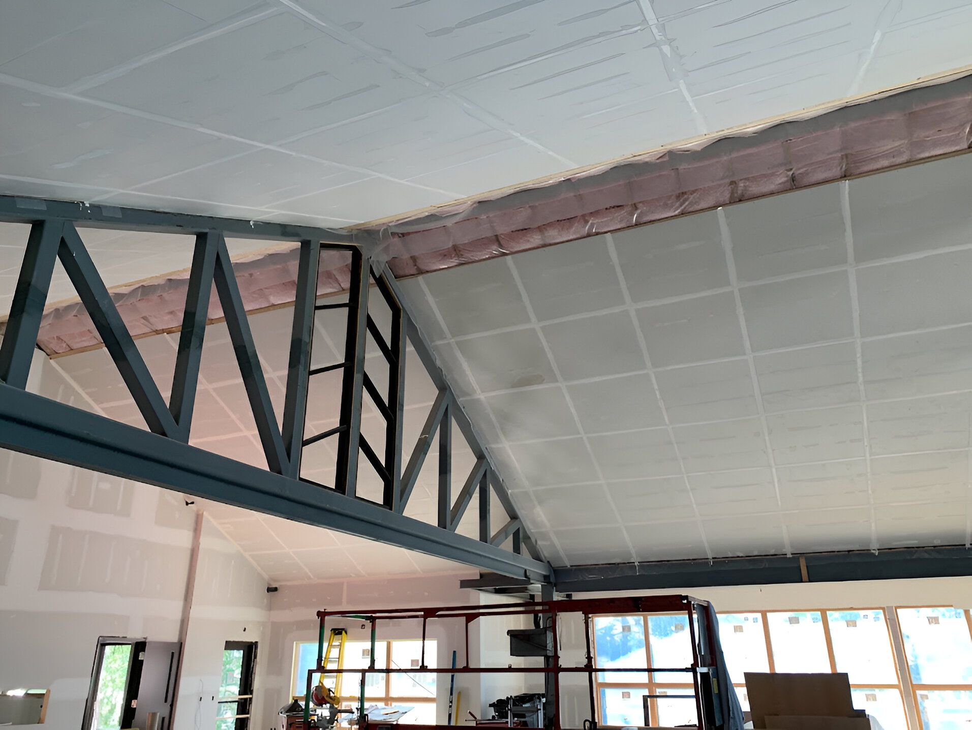 Interior construction: Ceiling with drywall, metal beams, pink insulation. Scissor lift in front of windows.