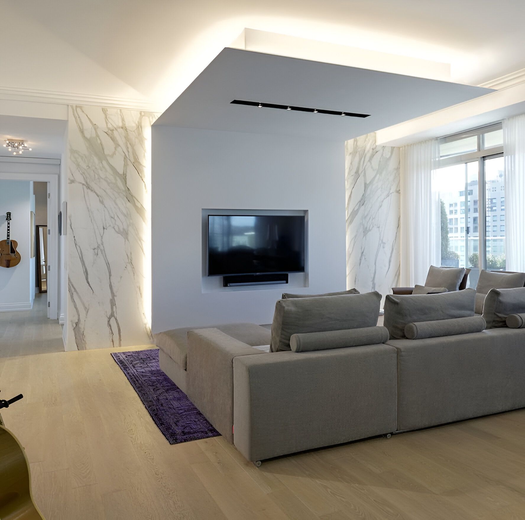 Spacious living room with gray sectional sofa, TV, marble columns, and light wood floors.
