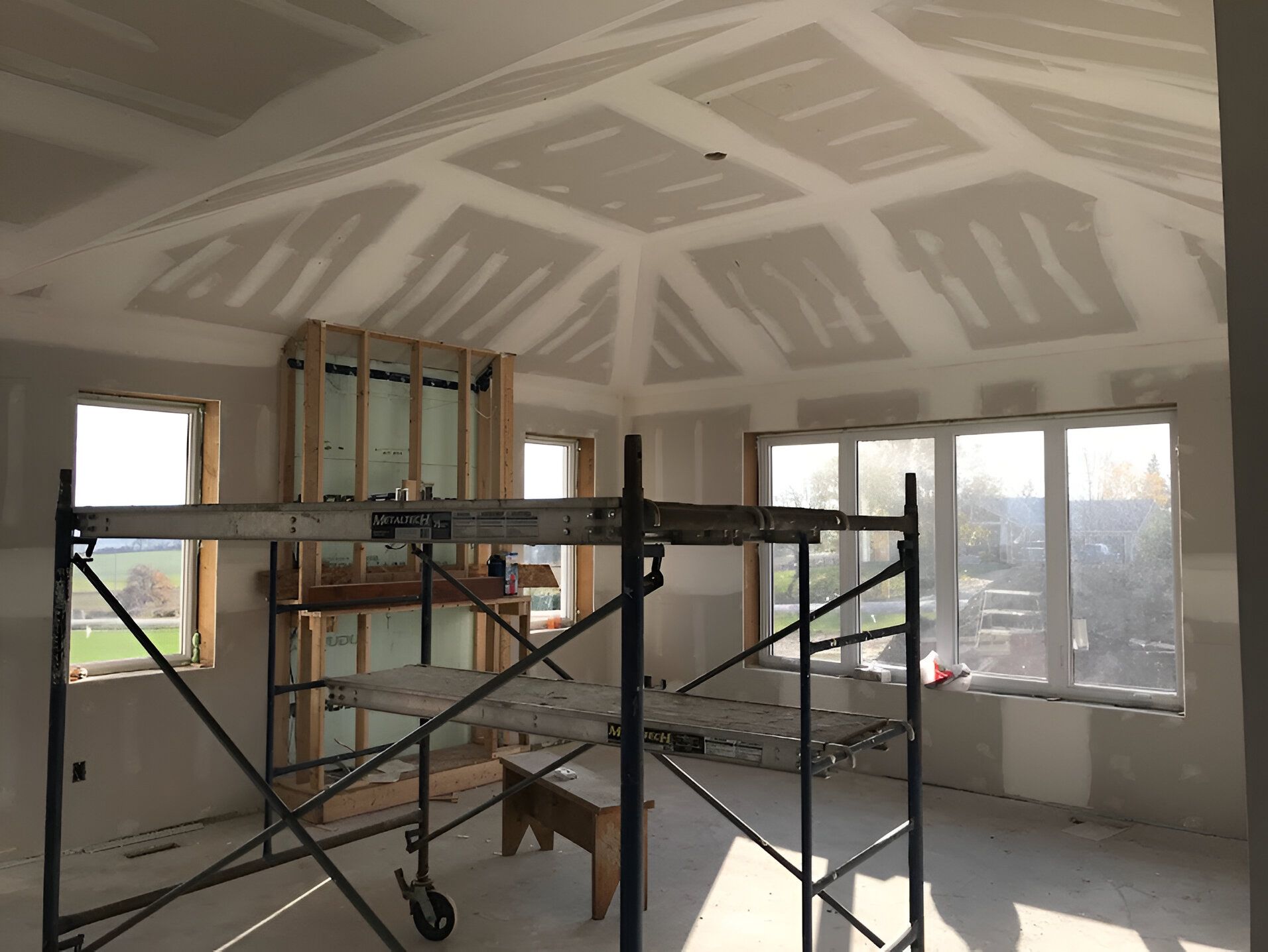 Interior room under construction with drywall on walls and ceiling, scaffolding present.