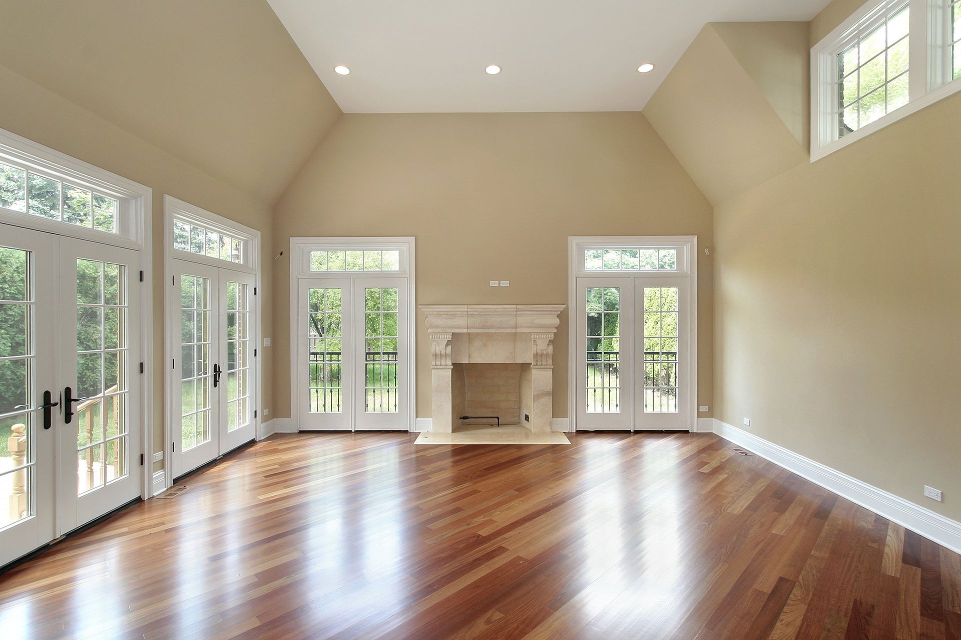 Empty room with hardwood floors, cream walls, fireplace, and French doors.