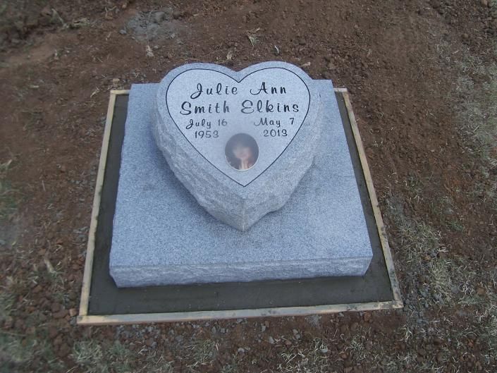 Gravestone with heart-shaped memorial plaque on a square stone base in a dirt cemetery plot