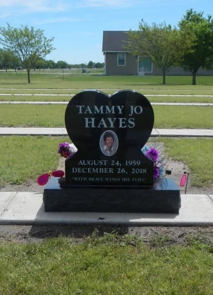 Black heart-shaped gravestone for Tammy Jo Hayes with flowers in a grassy cemetery.