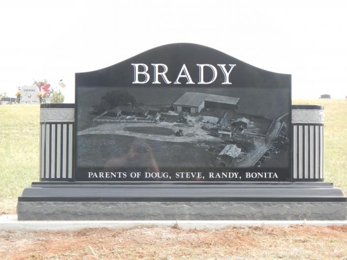 Black Brady family memorial gravestone with a rural farm scene engraving and engraved names at the base