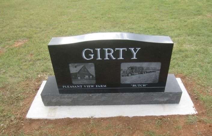 Black granite memorial headstone engraved “GIRTY” on a concrete base in a grassy cemetery.