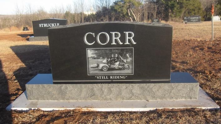 Black granite memorial headstone with “CORR” and a photo plaque in a cemetery